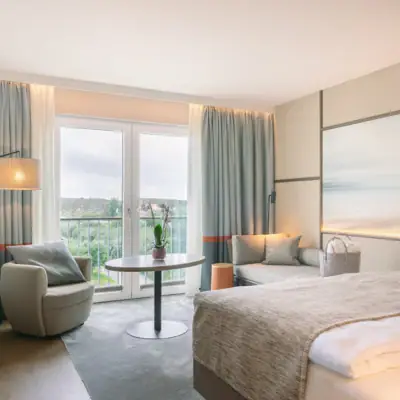 Zimmer im A-ROSA Sylt Zimmer mit Bett, Tisch und Stühlen.