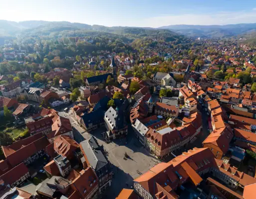 Wernigerode Luftaufnahme einer Stadt mit Häusern und Bäumen, im Hintergrund Berge und Himmel.