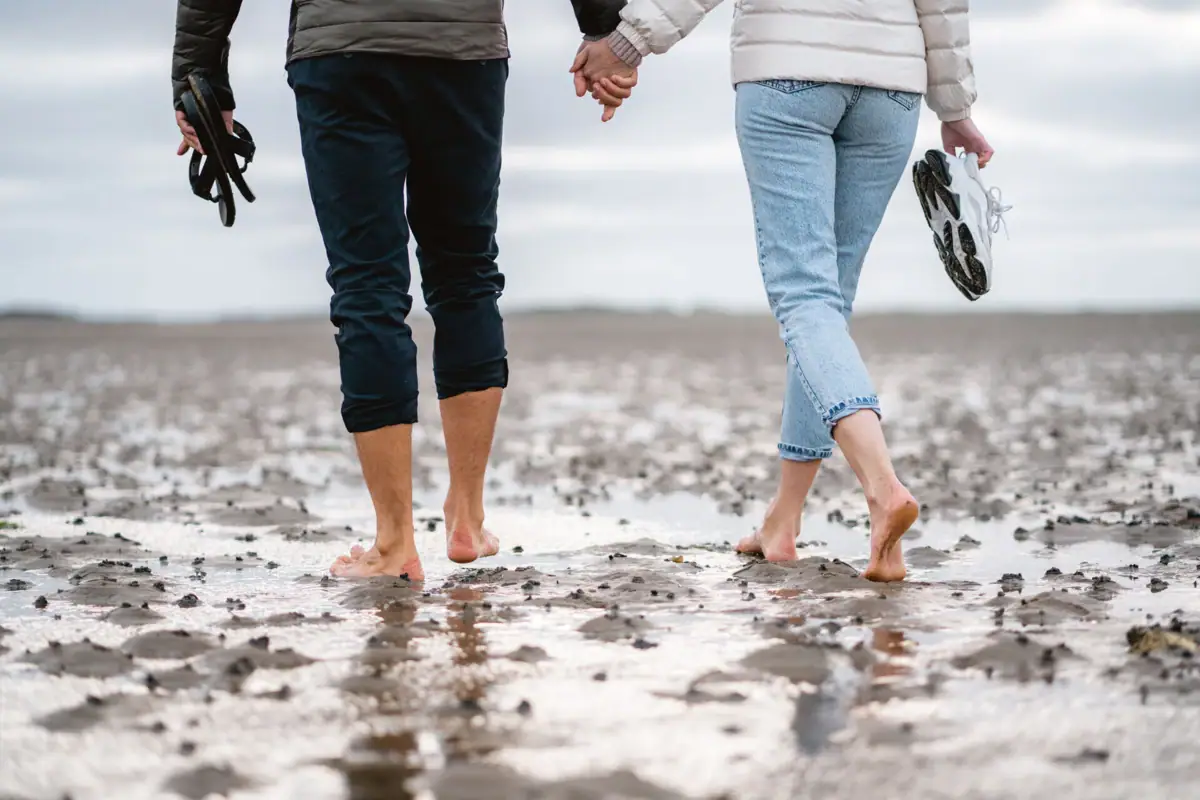 Ein Mann und eine Frau halten Händchen und gehen auf nassem Sand.