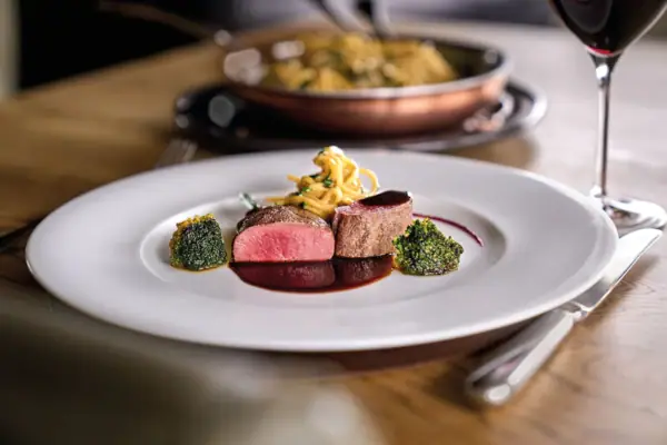 Walser Stube Carnozet im A-ROSA Ifen Hotel Kleinwalsertal Ein Teller mit kunstvoll angerichteter Speise auf einem Tisch.