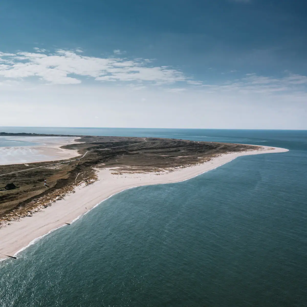 Ellenbogen Sylt Ein Strand mit Sand und Wasser unter einem bewölkten Himmel.