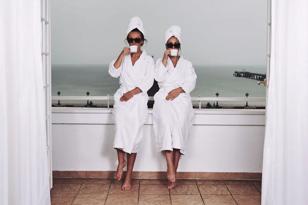 Zwei Frauen in weißen Bademänteln und Handtüchern sitzen auf einer Fensterbank.