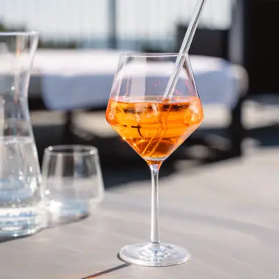 Ein Glas mit orangefarbener Flüssigkeit und Eis auf einem Tisch.