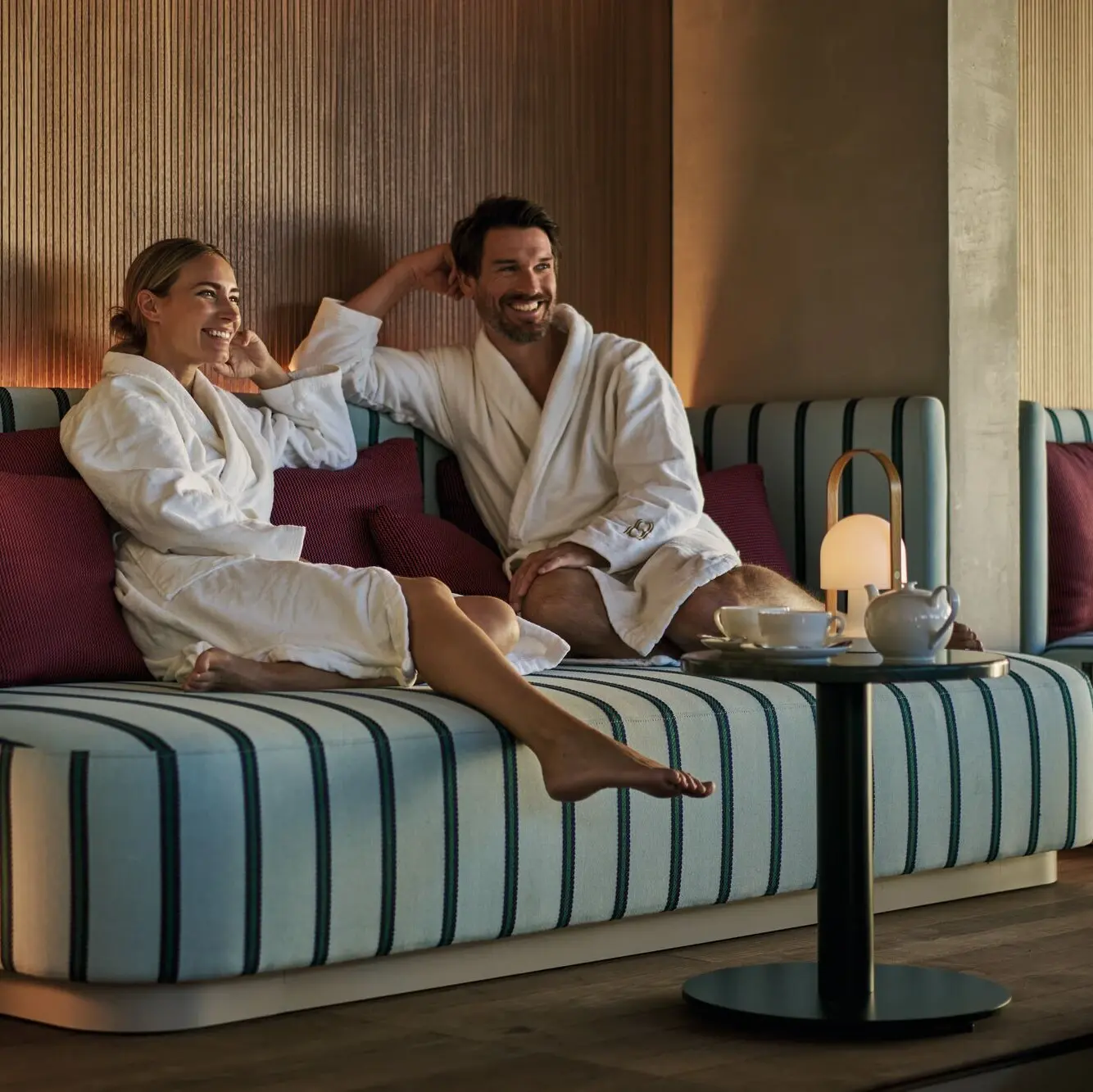 Mann und Frau sitzen in Bademäntel auf einer gemütlichen Sitzgelegenheit