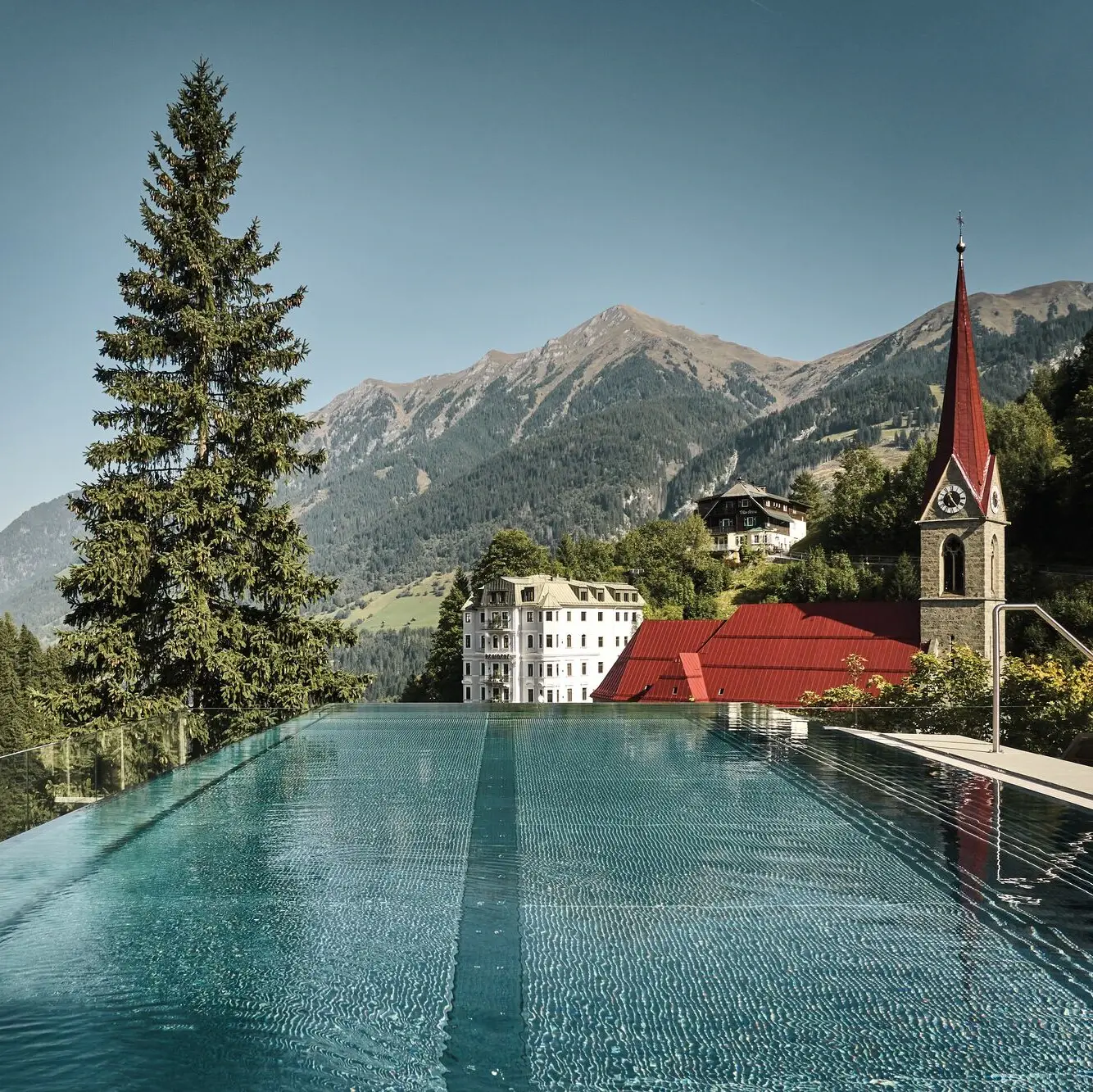 Infinity Pool mit Blick in die Berge Pool im Vordergrund, dahinter eine Kirche und eine Bergkette