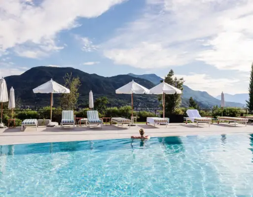 Eine Person im Pool mit Sonnenschirmen und Liegestühlen.