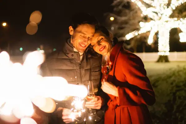 Silvester Travemünde Ein Mann und eine Frau halten Weingläser und lächeln einander an.
