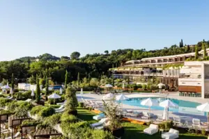 A-ROSA Hotel am Gardasee Ein Pool mit Sonnenschirmen und Liegestühlen vor einem Gebäude.