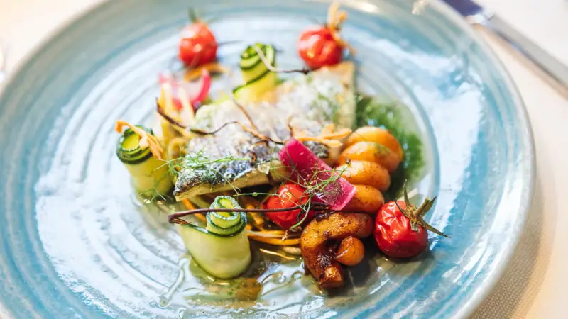 Abendessen im A-ROSA Gardasee Ein Teller mit kunstvoll angerichteter Speise auf einem Tisch.