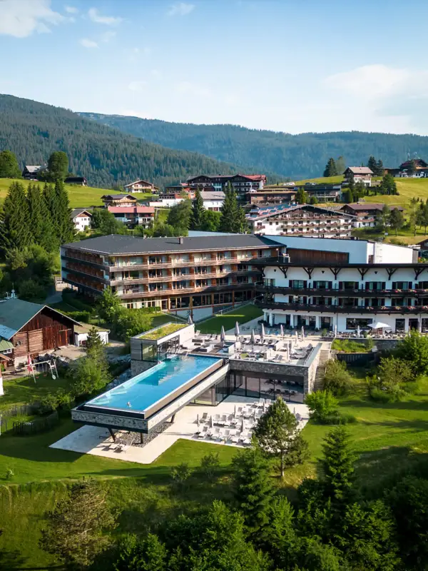 A-ROSA Kleinwalsertal Das A-ROSA Ifen Hotel Kleinwalsertal aus der Vogelperspektive mit einem Pool und Bergen im Hintergrund.