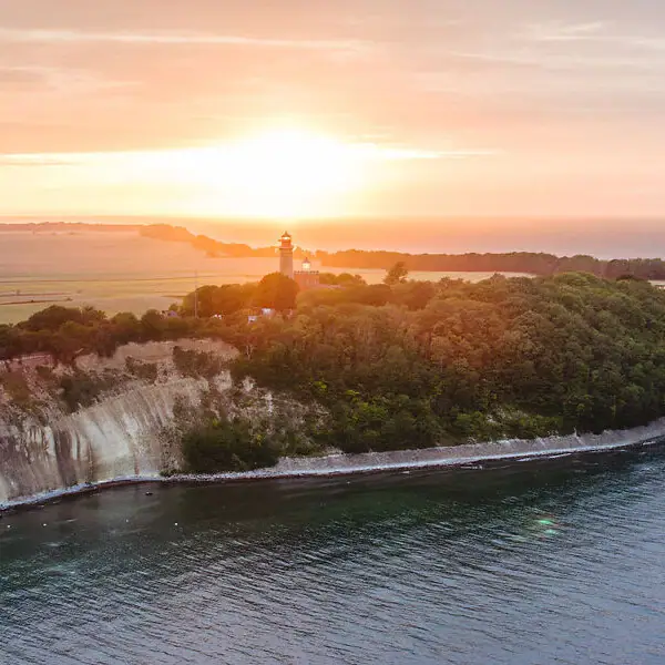 Ein Leuchtturm auf einem Hügel am Wasser.