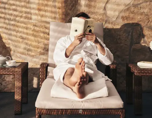 Eine Person liest ein Buch auf einem Stuhl liegend.