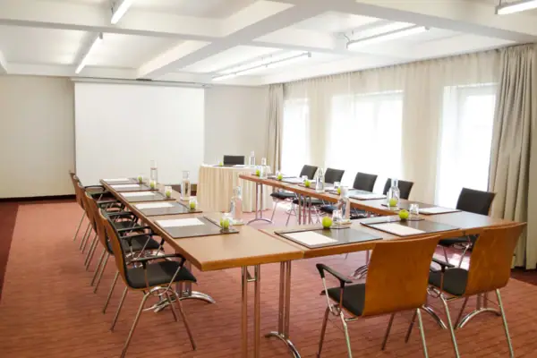 Tagungsraum Begegnung Ein Tagungsraum mit Tischen und Stühlen sowie einer Leinwand an der hinteren Wand.