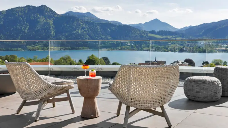A-ROSA Tegernsee Ein Tisch und Stühle auf einer Terrasse mit Blick auf ein Gewässer.