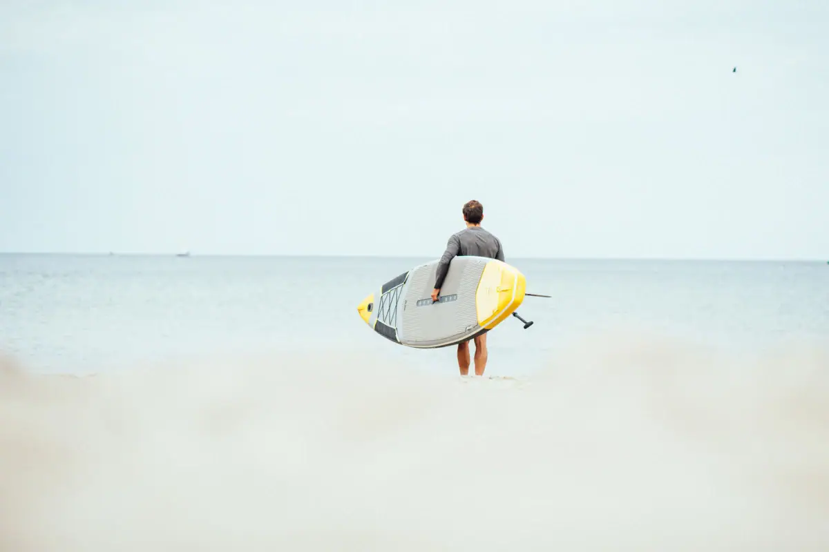 Ein Mann hält ein Surfbrett am Strand.