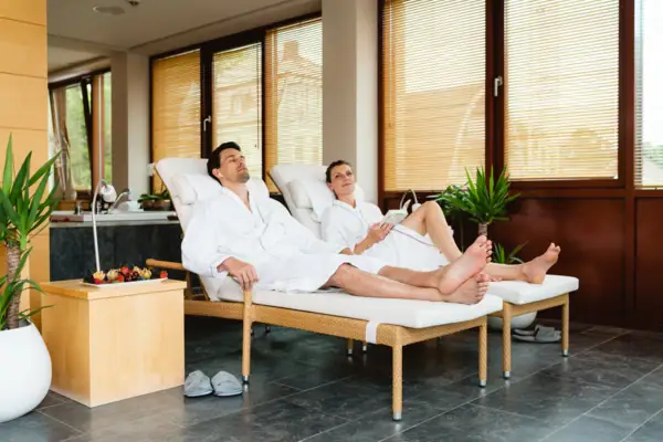 SPA-ROSA Travemünde Ein Mann und eine Frau in weißen Bademänteln liegen auf Liegestühlen.