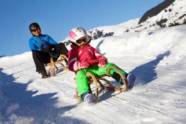 Ein Mann und ein Mädchen rodeln einen Hügel hinunter.