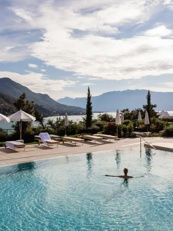 Eine Person im Pool mit Sonnenschirmen und Bergen im Hintergrund.
