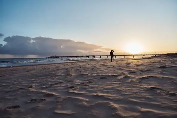 Eine Person steht am Strand unter einem bewölkten Himmel.