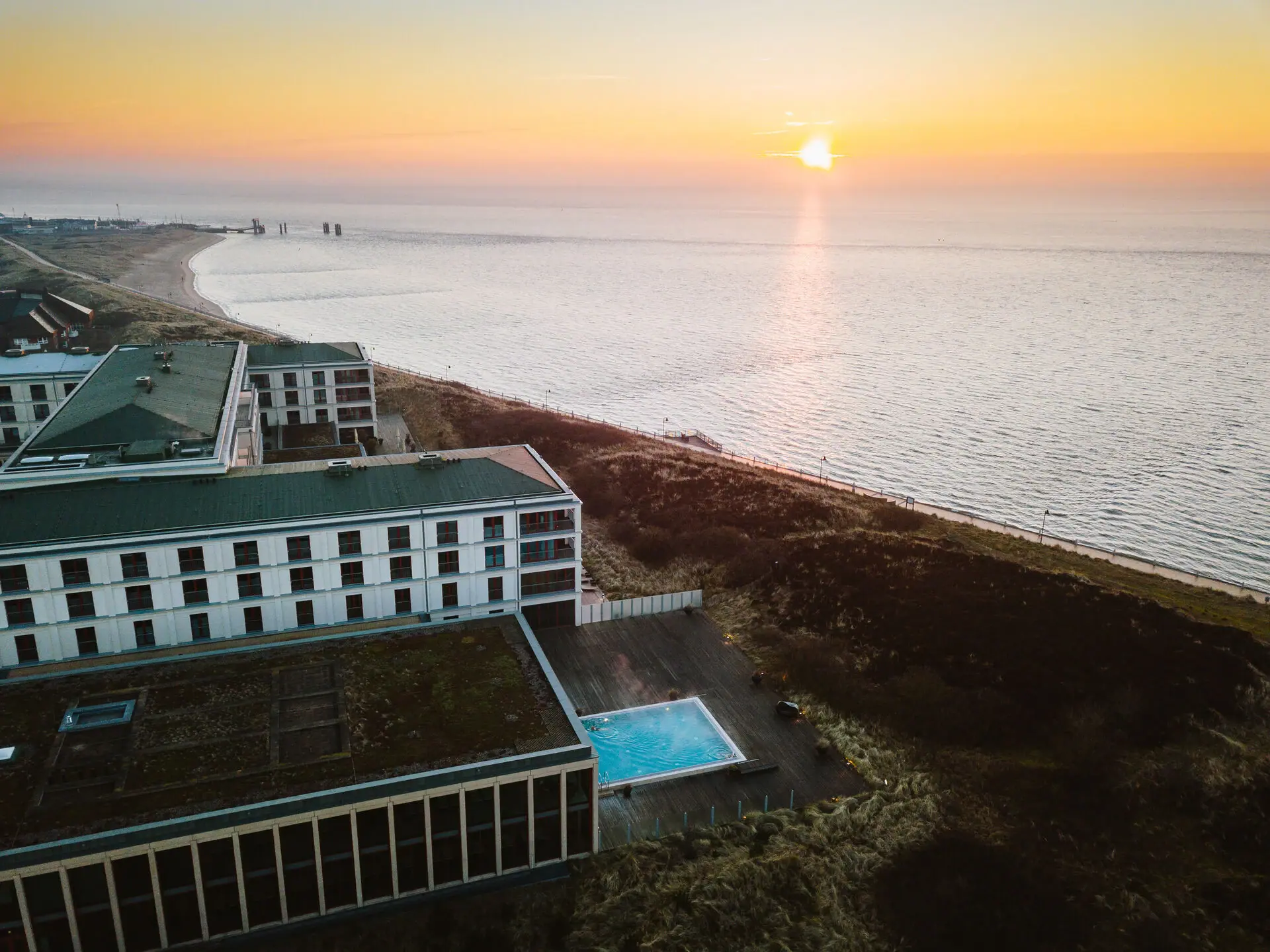 A-ROSA Sylt Ein Gebäude neben einem Strand bei Sonnenaufgang.