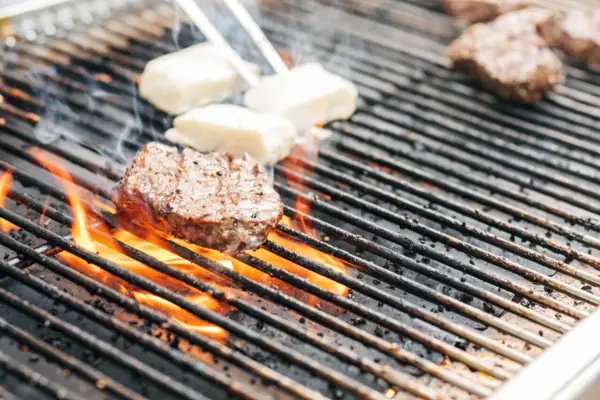 BBQ Ein Grill mit Fleisch und Käse darauf während eine Person mit einer Grillzange den Käse wendet.