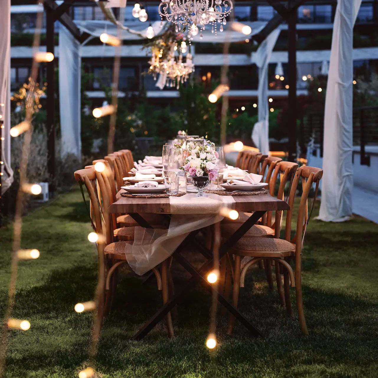 Ein Tisch für eine Abendgesellschaft gedeckt, mit Kerzen und Beleuchtung im Freien.