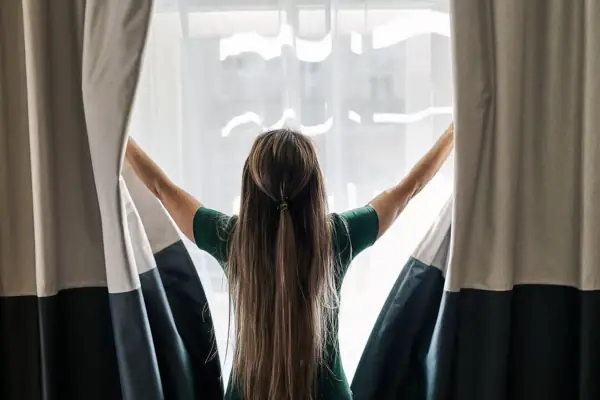 Eine Frau öffnet mit erhobenen Armen die Vorhänge.