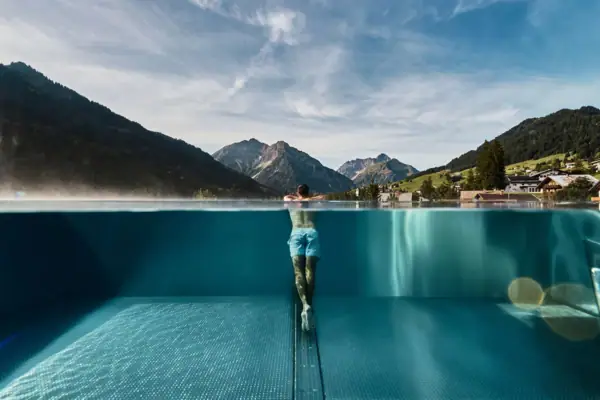 Außenpool Ein Mann in einem Pool mit Bergen im Hintergrund.