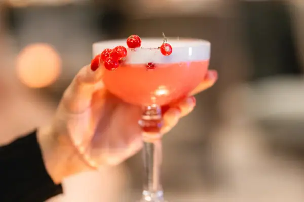 Cocktail Eine Hand hält ein Glas mit rosa Flüssigkeit.