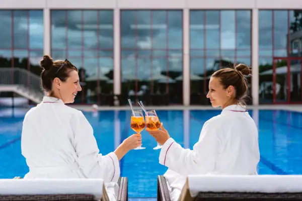 SPA-ROSA Travemünde Zwei Frauen in weißen Bademänteln halten Getränke.