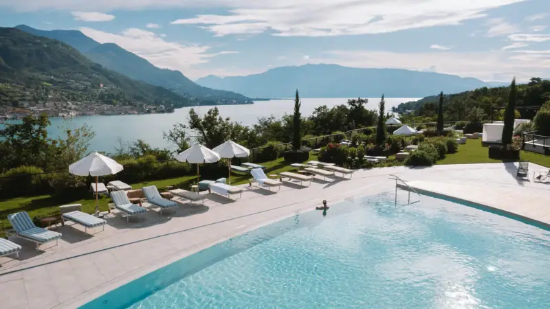 Gartenpool im A-ROSA Gardasee Ein Pool mit Liegestühlen und Sonnenschirmen am Wasser.