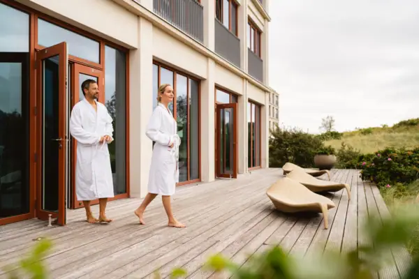 Ein Mann und eine Frau in weißen Bademänteln gehen auf einem Deck spazieren.