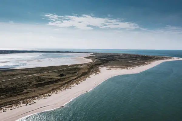 Strand mit Sand und Wasser unter bewölktem Himmel.
