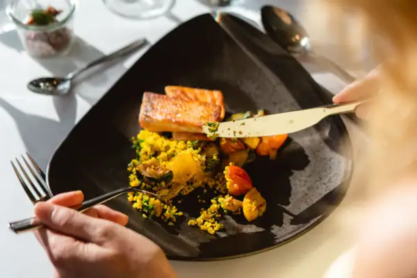 Hochzeitsmenüs Eine Frau mit blonden Haaren isst mit Messer und Gabel von einem Teller.