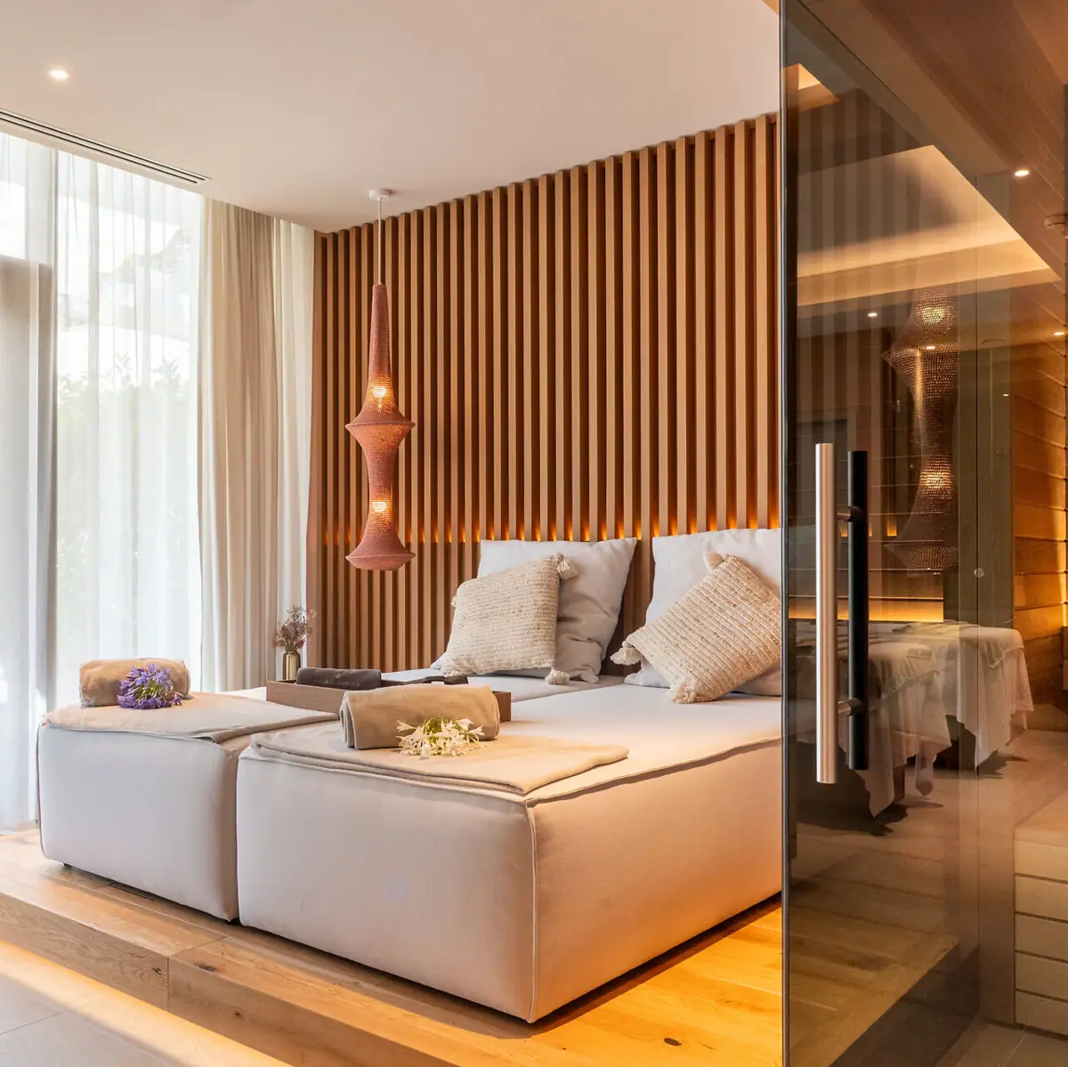 Ein Zimmer mit einem Day-Bed und einer Sauna mit einer Glastr getrennt.