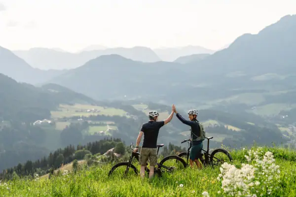 Fahrradtour Zwei Personen stehen in einer Berglandschaft mit ihren fahhrädern und geben sich ein Highfive.