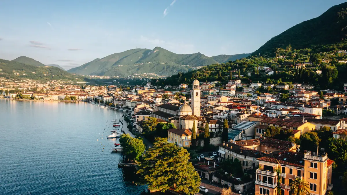 Stadt am Ufer eines Sees mit Bergen im Hintergrund.