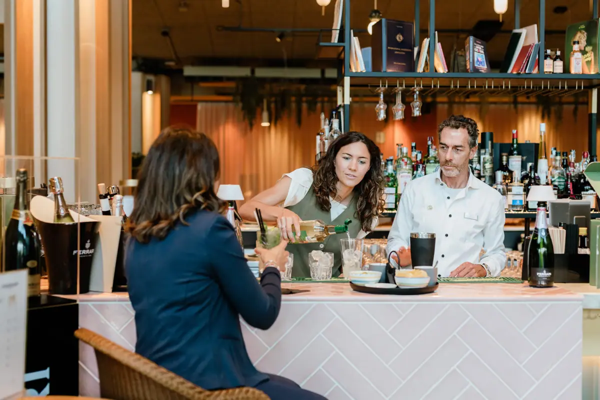 cocktail masterclass Eine Frau schenkt einer anderen Frau an einer Bar ein Getränk ein.
