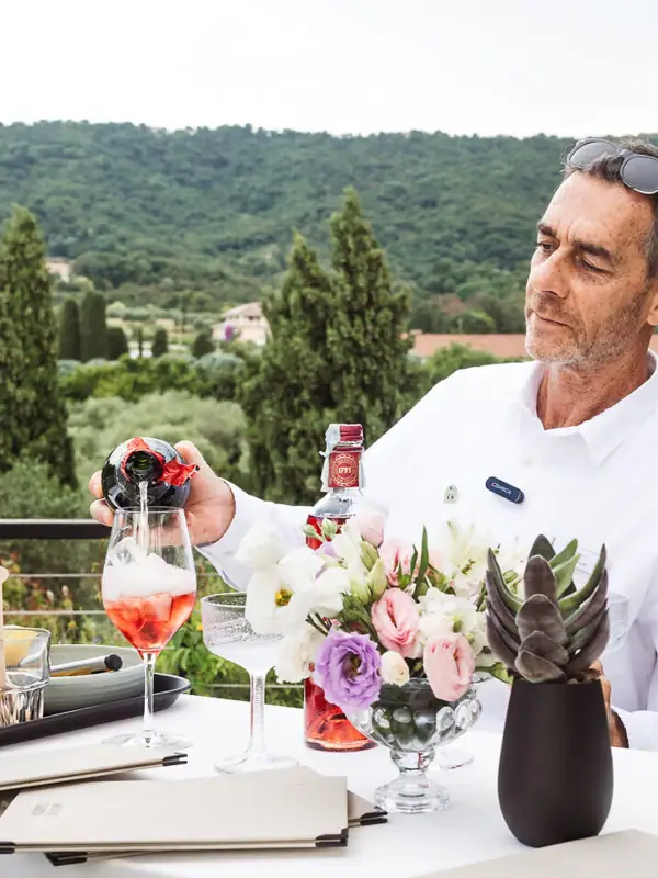 Ein Mann steht an einem Tisch mit einer Weinflasche und Blumen.