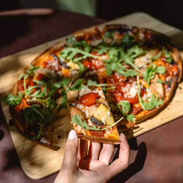 Tellerwerk Eine Hand hält ein Stück Pizza.