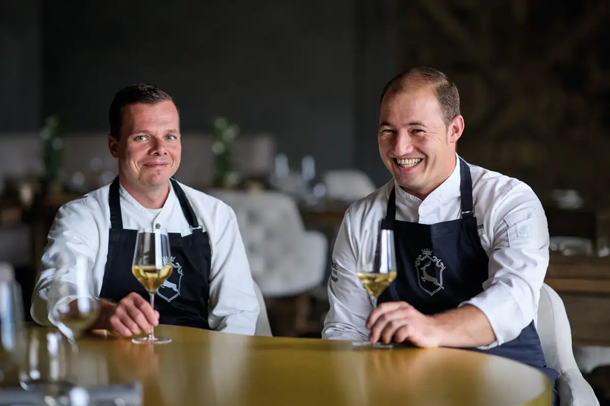 Hansjörg Frick & Sascha Kemmerer Gruppe von Männern in schwarzen Schürzen, die Weingläser halten.
