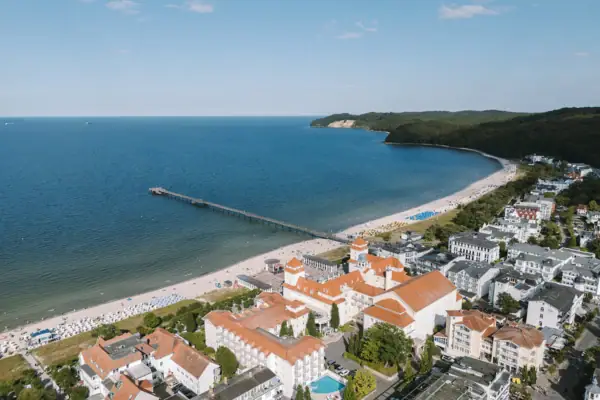 Kurhaus Binz Außenansicht Strand mit Gebäuden und einem Pier im Vordergrund.