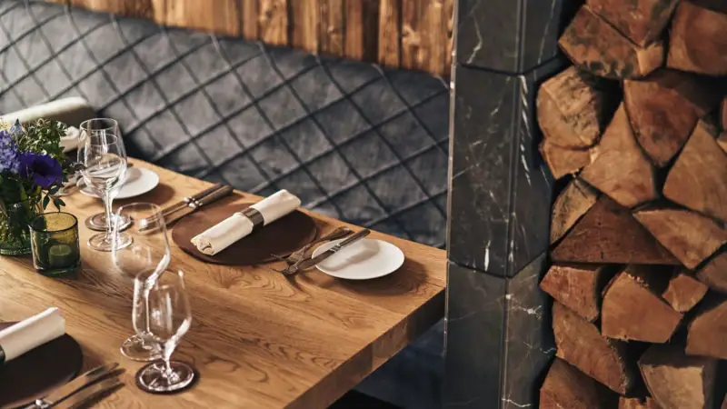 Ein Tisch mit Tischgeschirr, einer Vase und Weingläsern vor einer Holzwand und einem Stapel Holz.