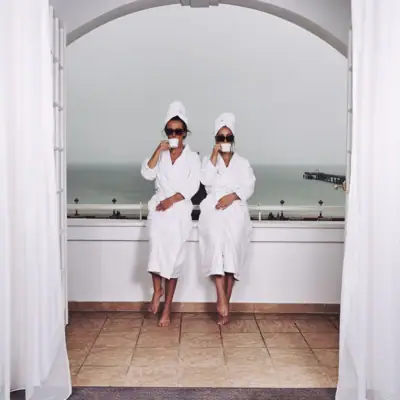 Zwei Frauen in weißen Bademänteln und Handtüchern sitzen auf einer Fensterbank.