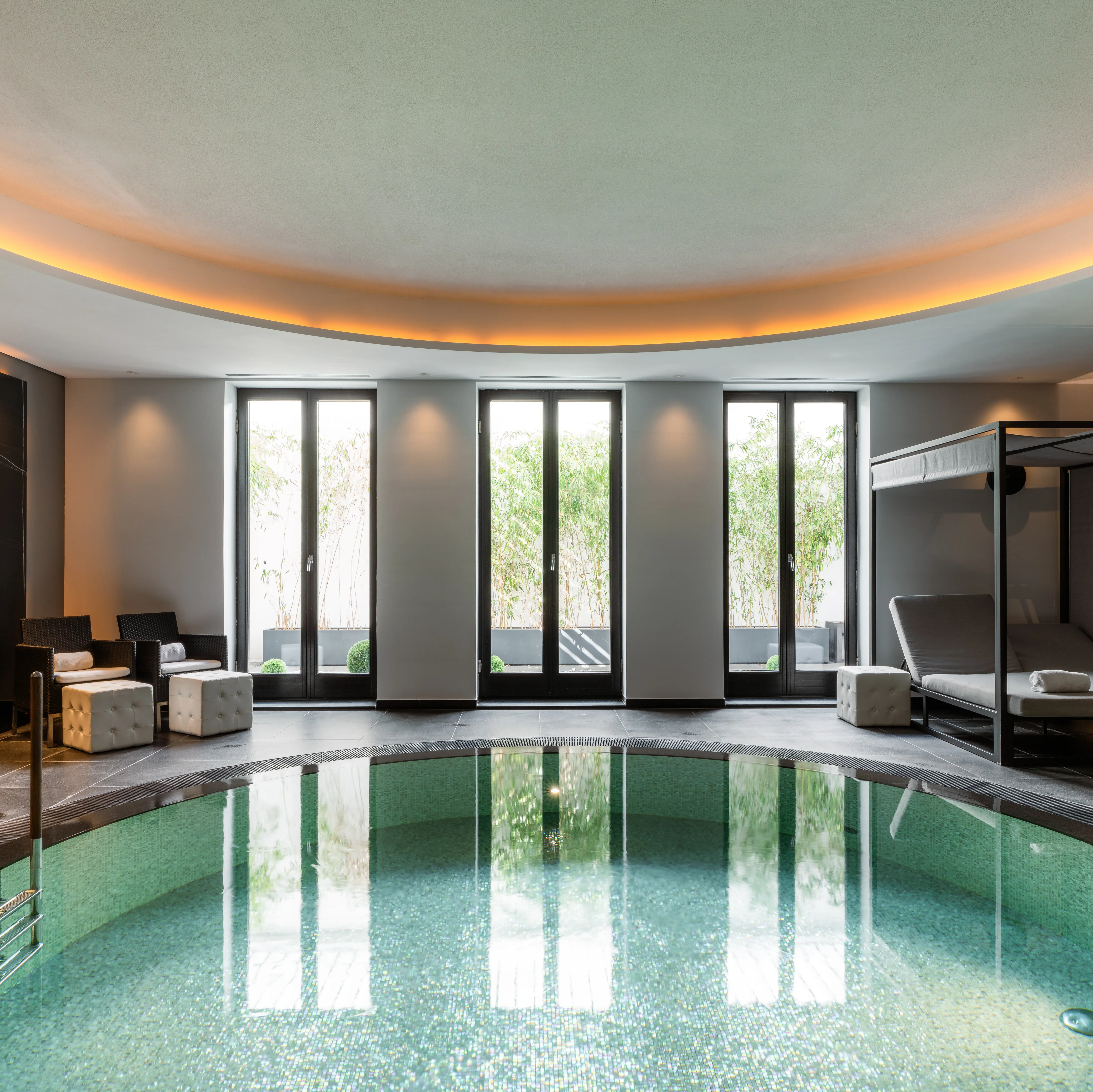 Ceres Pool Ein runder Pool mit blauem Wasser vor einer Fensterwand mit Blick ins Grüne.