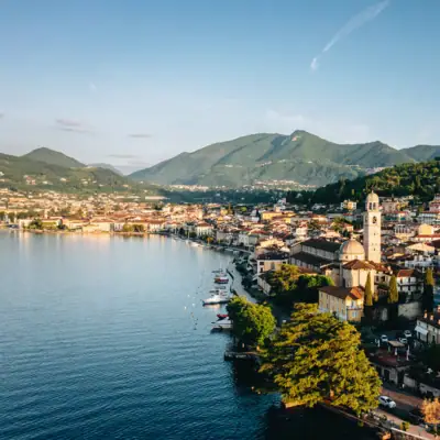 Stadt am Wasser mit Bergen im Hintergrund und vereinzelten Häusern entlang des Ufers.