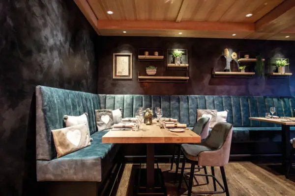 Restaurant Theo's im Ifen Hotel Kleinwalsertal Ein Tisch mit Stühlen und einer gepolsterten Sitzbank, darauf Teller und Gläser, in einem stilvoll eingerichteten Raum.