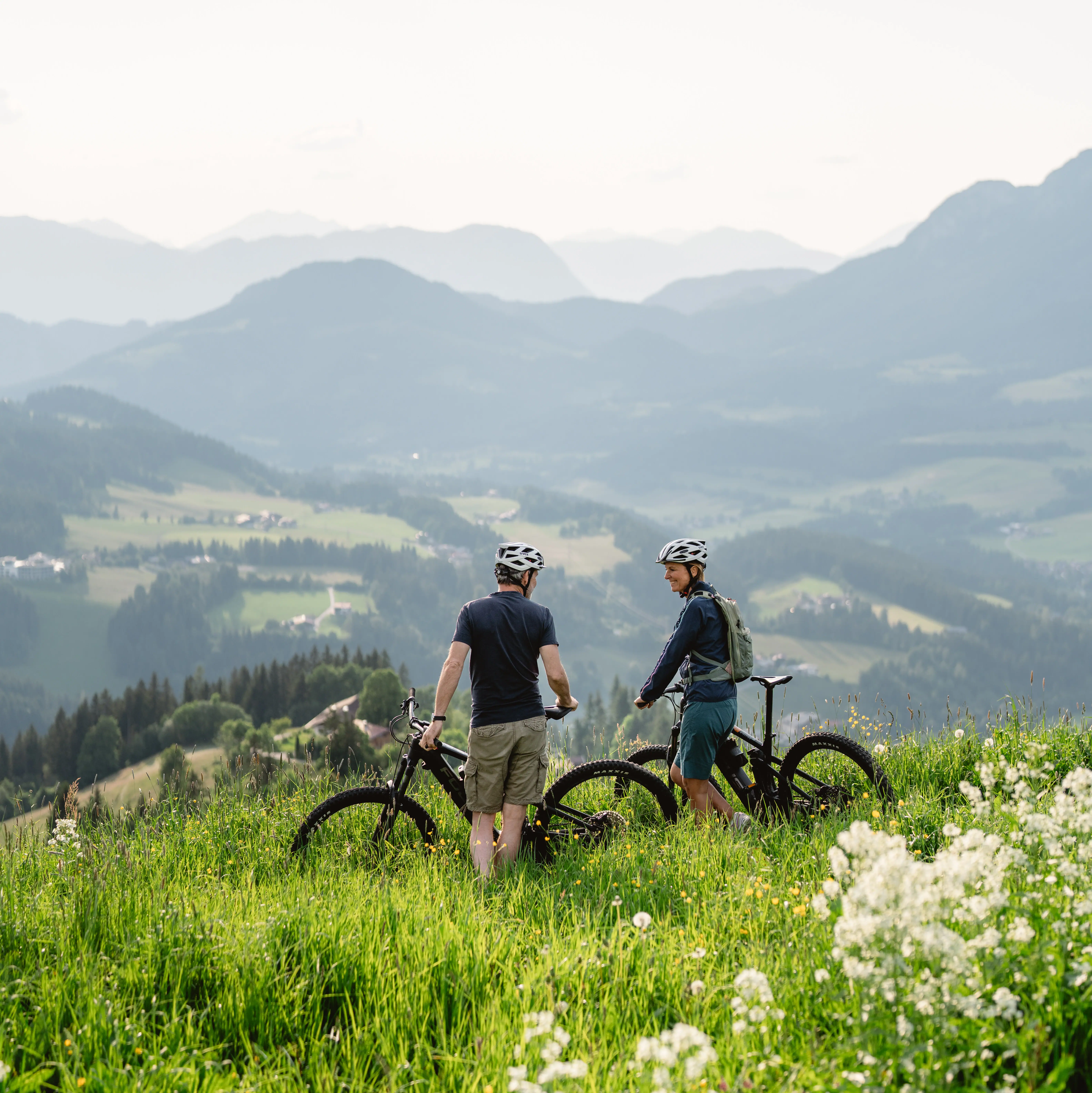 Zwei Radfahrer stehen oben auf einer grünen Wiese auf einem Berg.