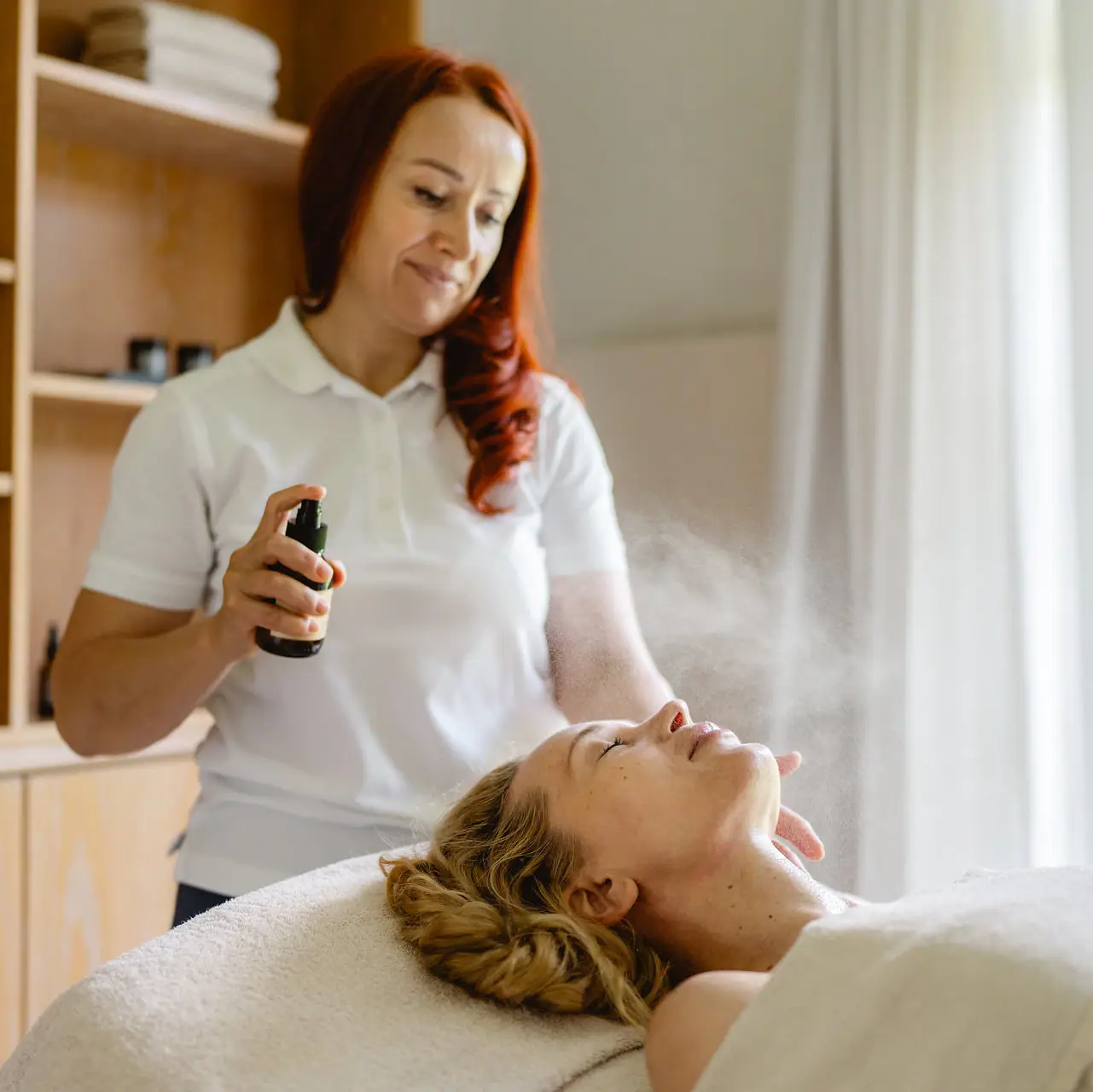 Eine Frau sprüht ein Gesichtsspray auf.