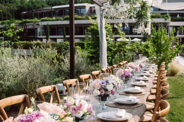 Outdoor-Hochzeitstafel am Gardasee Lange Hochzeitstafel im Garten, dekoriert mit rosa und weißen Blumen, Holzstühlen und Blick ins Grüne.